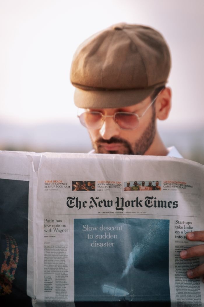 A man intently reads a newspaper outdoors on a sunny day, focused and thoughtful.